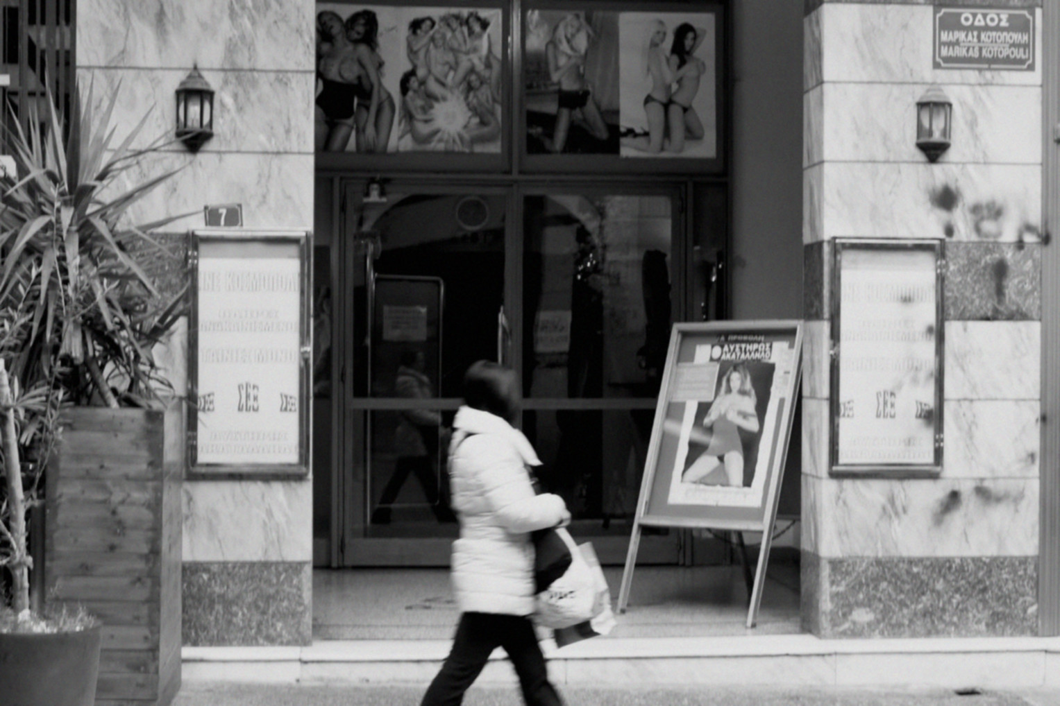 Une femme passe devant un théâtre / showroom X avec des affiches de scènes lesbiennes hardcore.