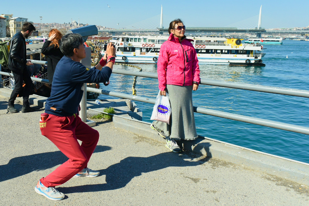 Un homme asiatique plie les genoux pour photographier sa compagne, qui pose au bord de l'eau à Istanbul
