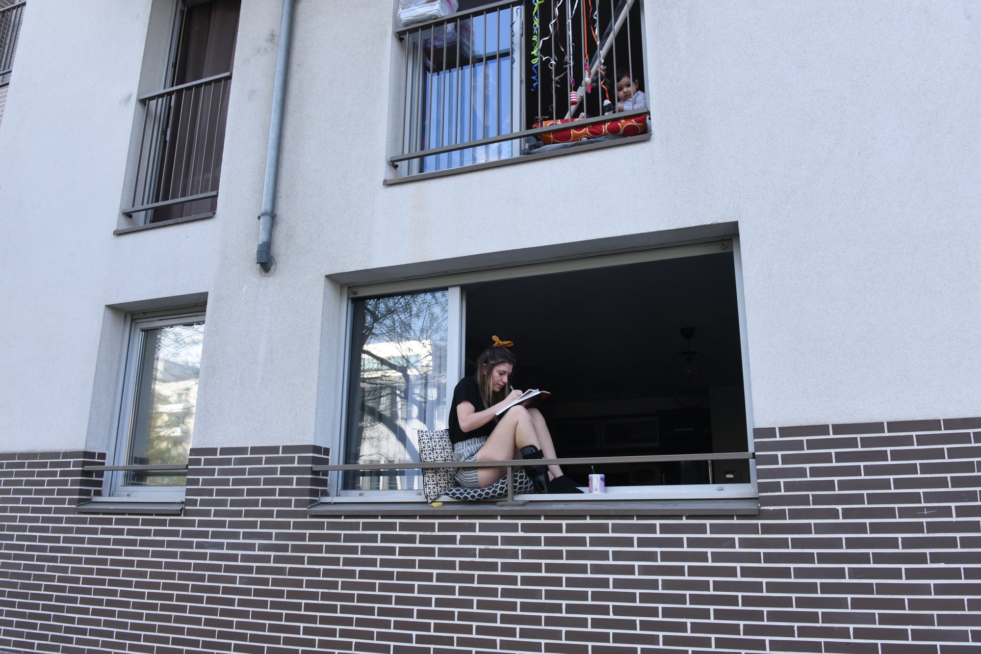 Jeune fille et bébé à la fenêtre, durant le confinement obligatoire pour cause d'épidémie de coronavirus